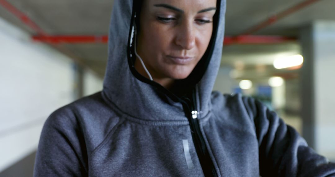 Focused Woman in Hoodie with Earphones Checking Fitness Tracker in Urban Setting - Free Images, Stock Photos and Pictures on Pikwizard.com