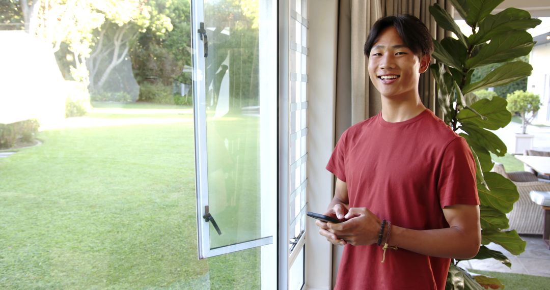 Smiling Teen Boy Using Smartphone by Open Sliding Door at Home