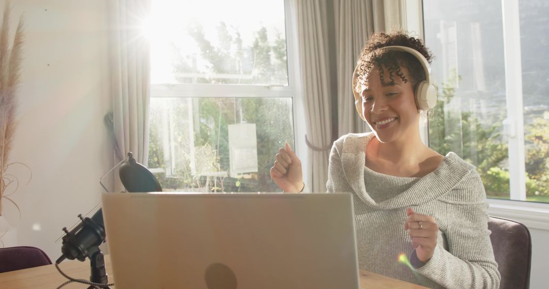 Smiling woman recording podcast at home studio with laptop, microphone and sunlight