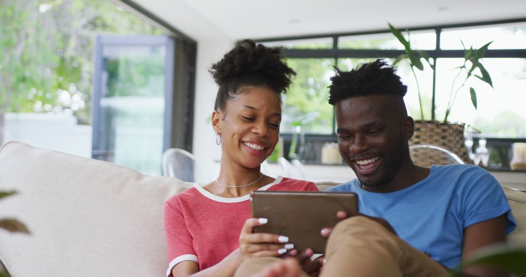 Image of happy african american couple sitting on sofa and using tablet - Free Images, Stock Photos and Pictures on Pikwizard.com