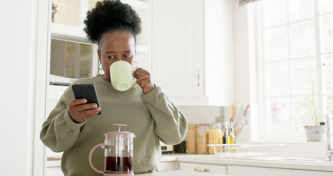 Woman Drinking Coffee while Using Smartphone in Bright Kitchen - Free Images, Stock Photos and Pictures on Pikwizard.com