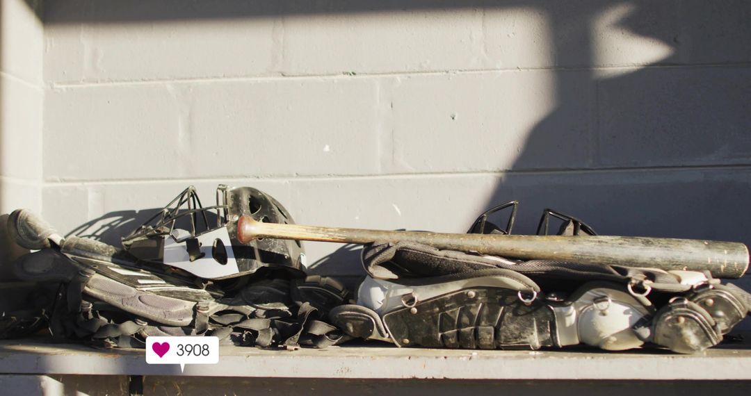 Worn catcher gear and bat stacked on bench against cinderblock wall with social like badge