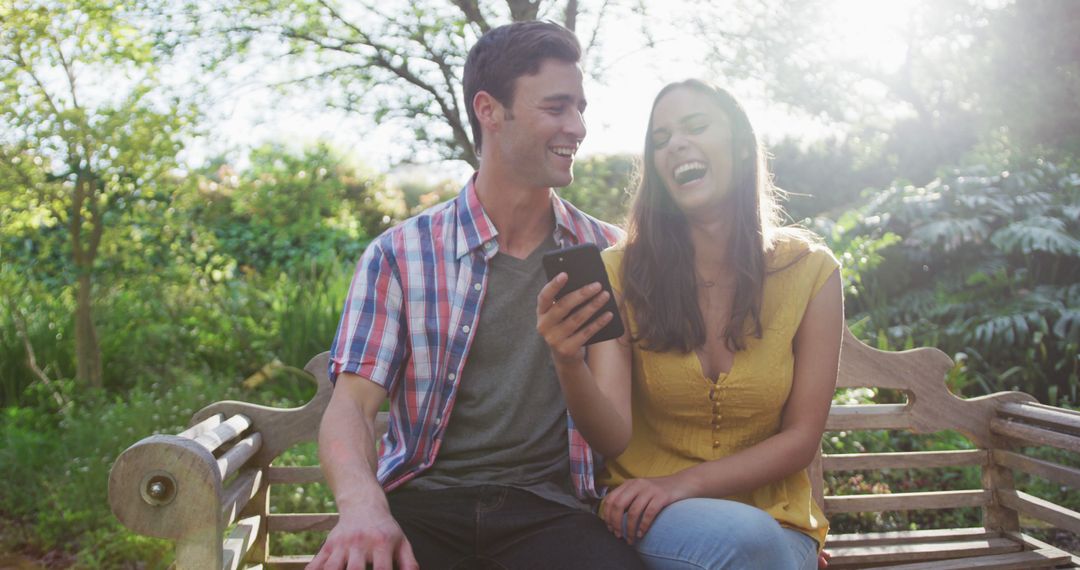 Happy couple on bench using smartphone in sunny park