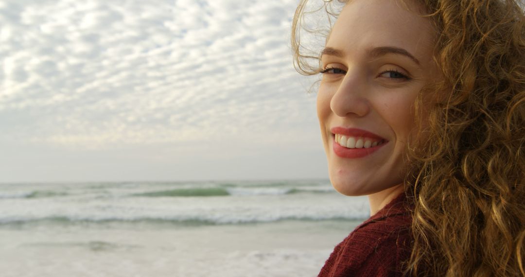 Young Woman Smiling at Beach With Wavy Clouds in Sky - Free Images, Stock Photos and Pictures on Pikwizard.com