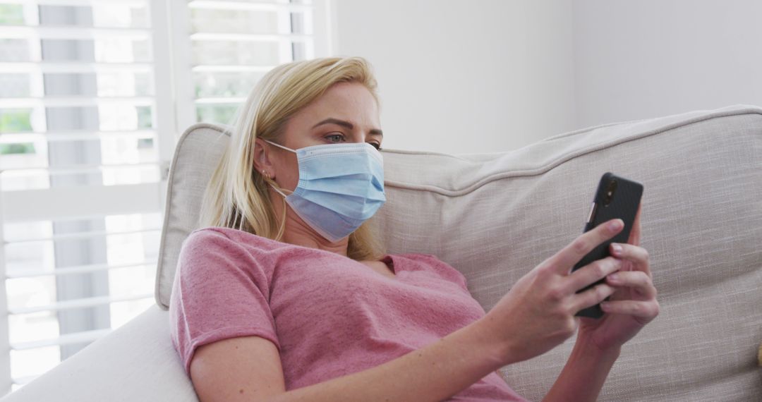 Young Woman Relaxing on Sofa Wearing Protective Face Mask and Using Smartphone - Free Images, Stock Photos and Pictures on Pikwizard.com