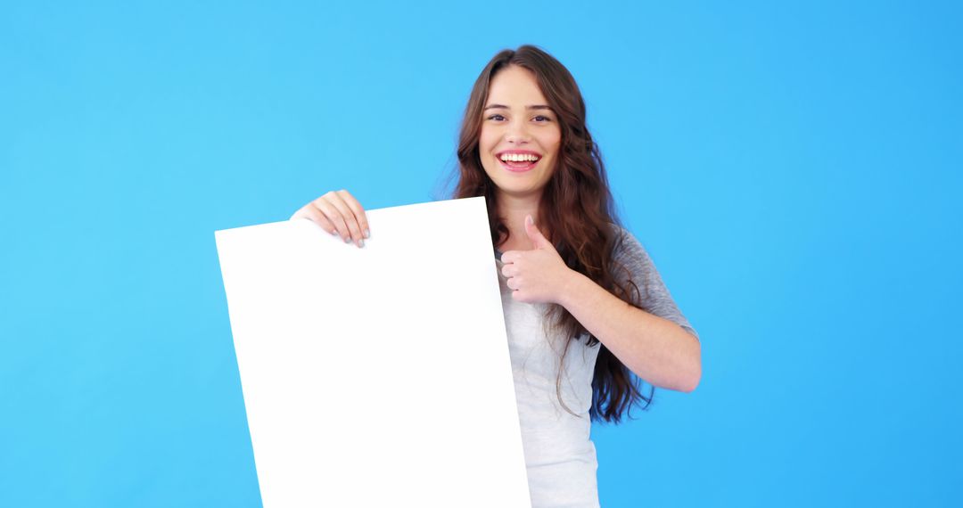 Smiling Woman Holding Blank White Sign Thumbs-up on Blue Background - Free Images, Stock Photos and Pictures on Pikwizard.com