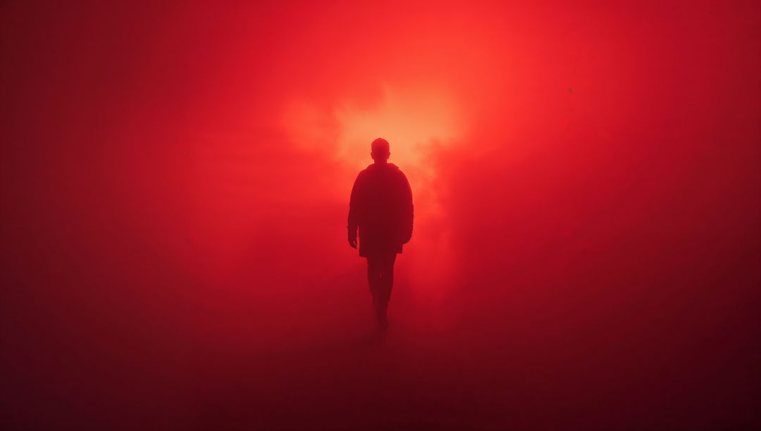 Silhouetted Man Walks Toward Red Light in Foggy Atmosphere