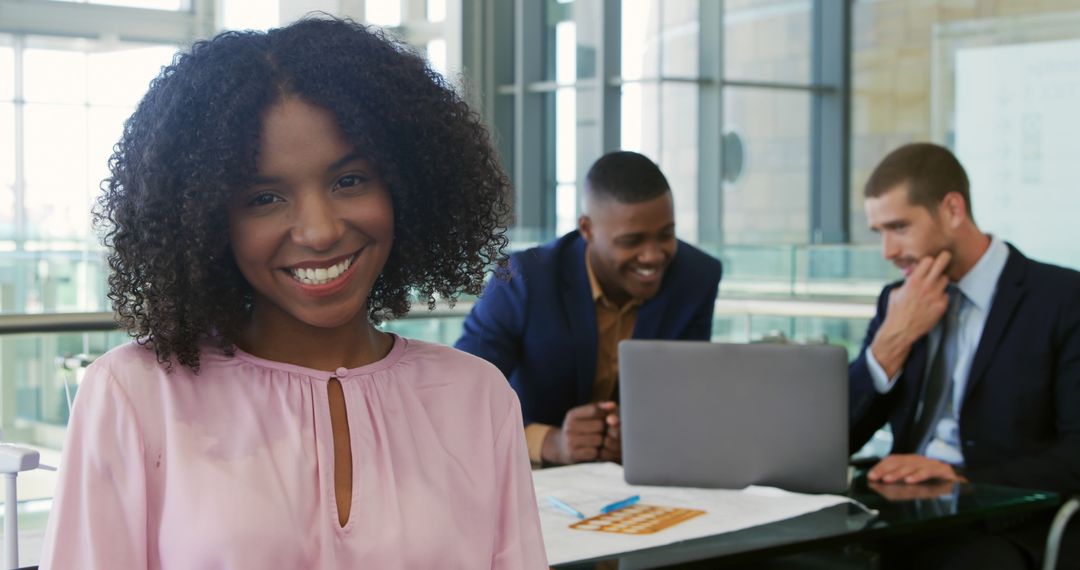 Confident Businesswoman Smiling in Modern Office with Colleagues Working in Background - Free Images, Stock Photos and Pictures on Pikwizard.com