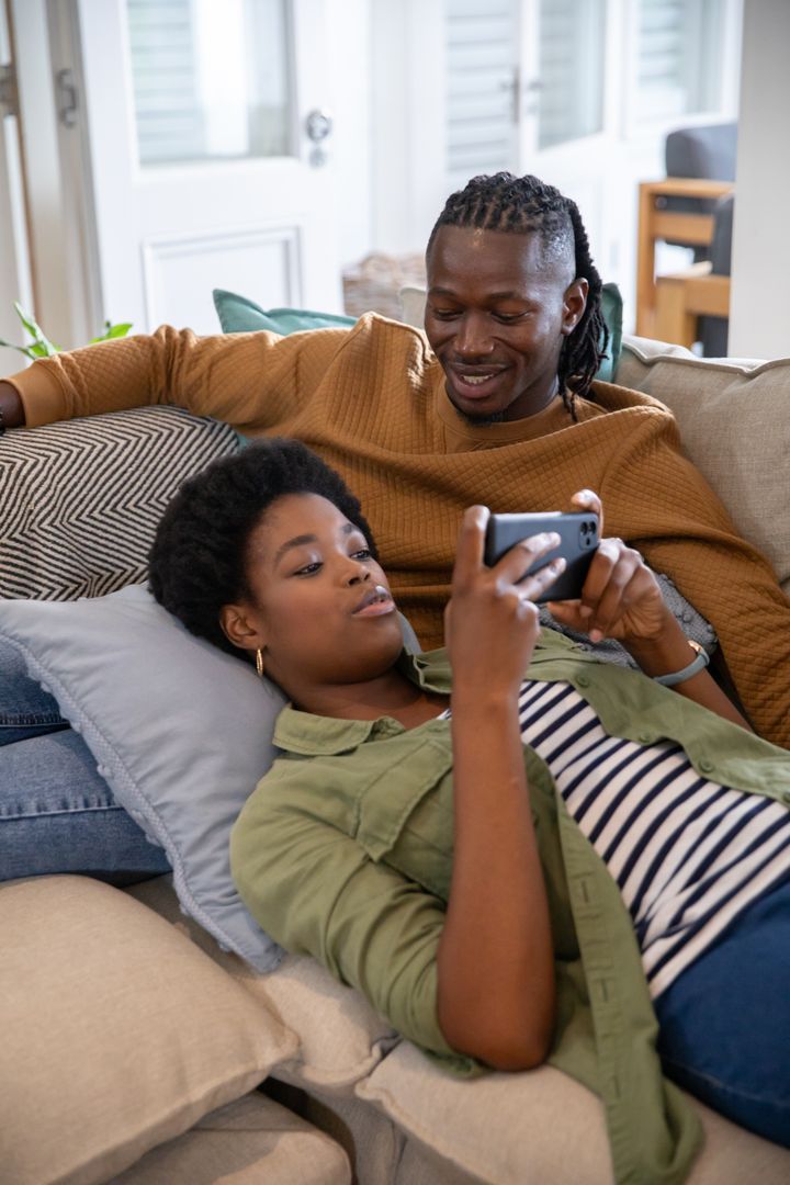 African American Couple Relaxing on Sofa with Smartphone