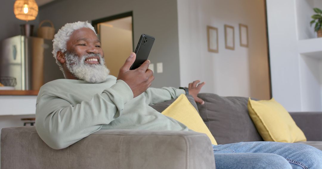Senior Man Relaxing on Sofa with Smartphone in Modern Home