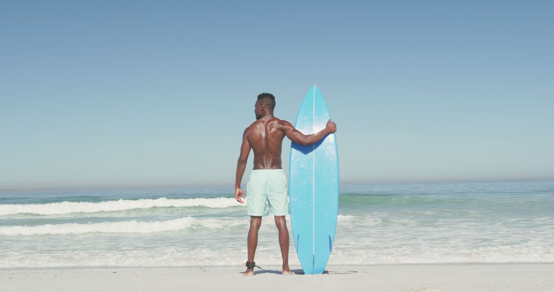 Back view african american man standing on beach with surfboard and looking on sea - Free Images, Stock Photos and Pictures on Pikwizard.com