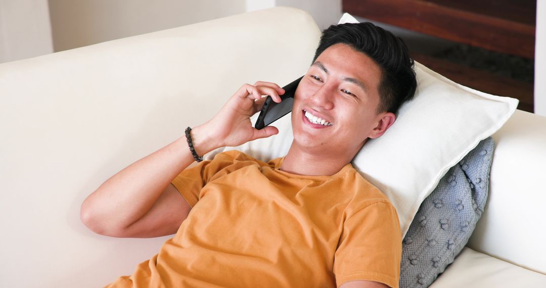 Smiling Young Man Pleasantly Talking on Smartphone at Home