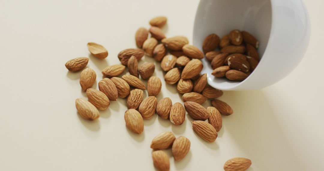 Almonds Scattered from Bowl on Light Surface