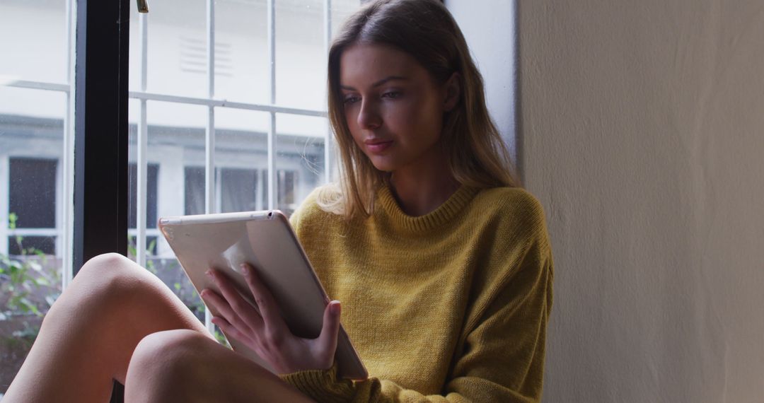 Young Woman Relaxing Near Window Reading Tablet - Free Images, Stock Photos and Pictures on Pikwizard.com