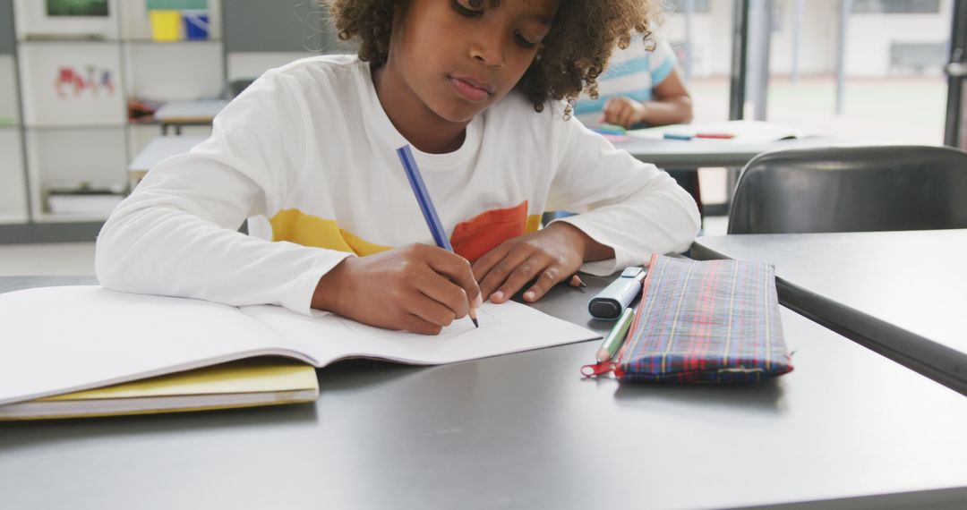 Image of african american schoolboy sitting at desk writing in school class - Free Images, Stock Photos and Pictures on Pikwizard.com