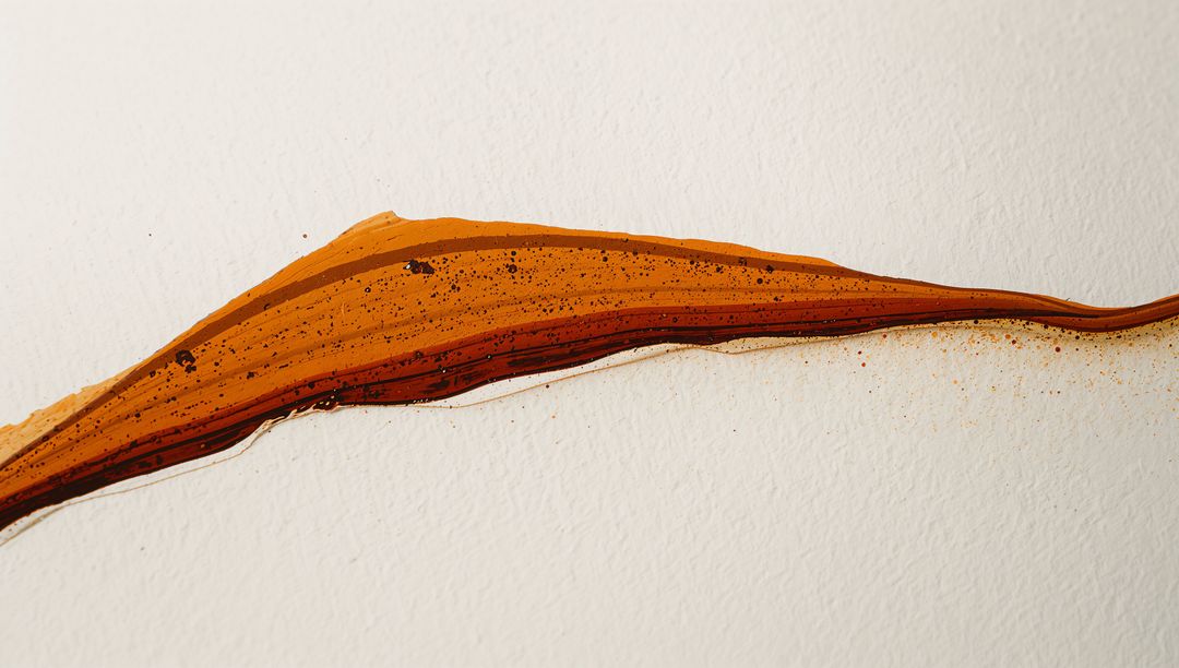 Amber Rust Brush Stroke Flowing Across Textured Paper with Pigment Splatter Detail