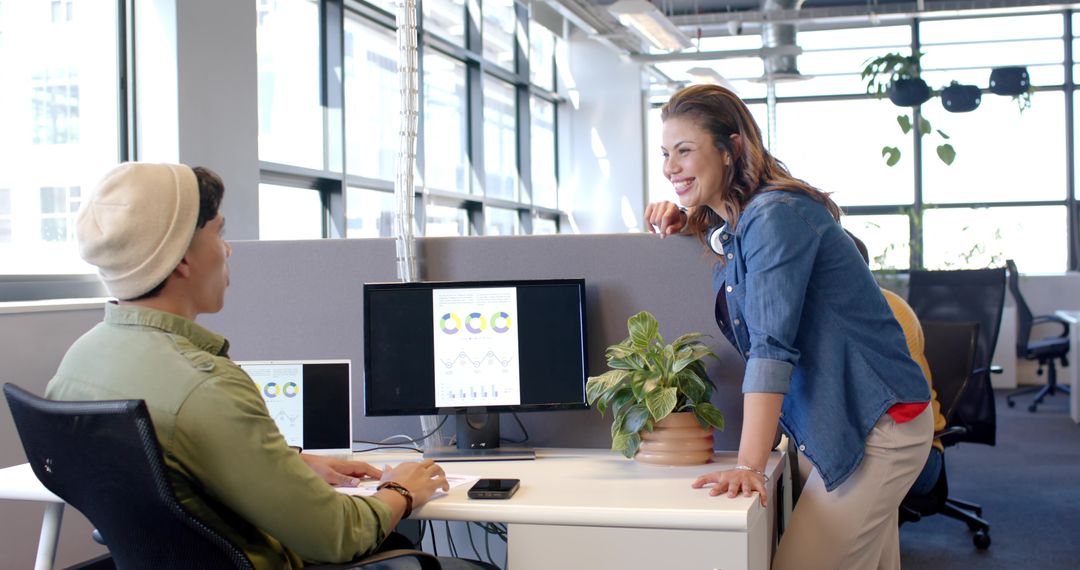 Smiling coworkers collaborating at open-plan office desk with charts on monitor and smartphone