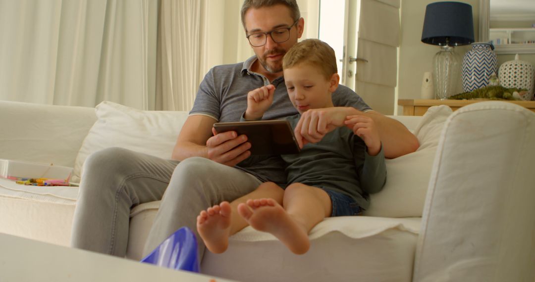 Father and Son Using Tablet on Couch in Living Room - Free Images, Stock Photos and Pictures on Pikwizard.com