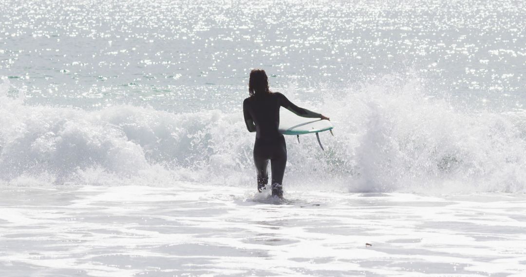 Rear view of biracial woman walking into the sea carrying surfboard - Free Images, Stock Photos and Pictures on Pikwizard.com
