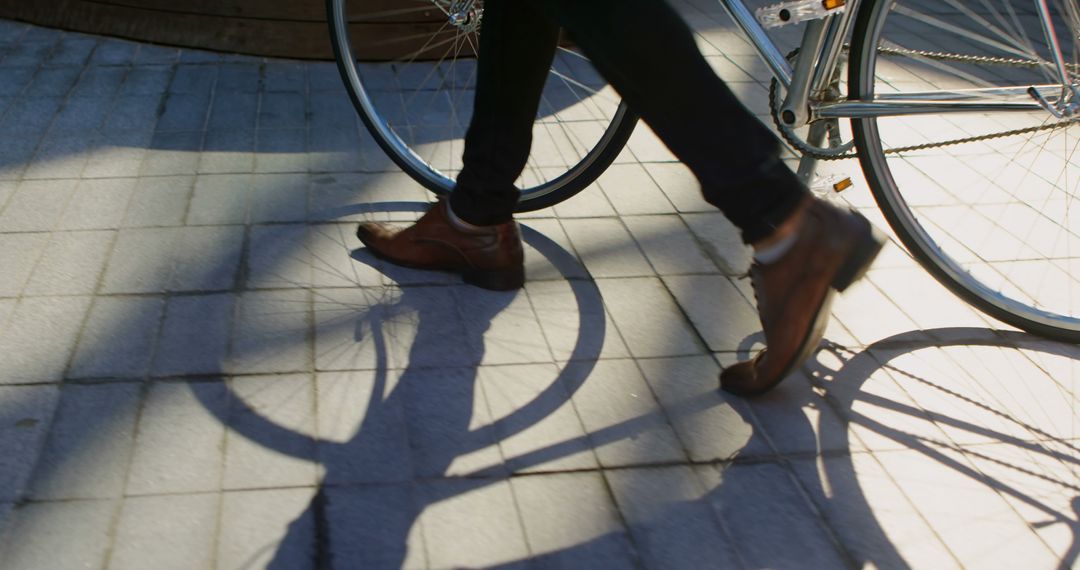 Person Walking Next to Bicycle on Sunlit Pavement - Free Images, Stock Photos and Pictures on Pikwizard.com