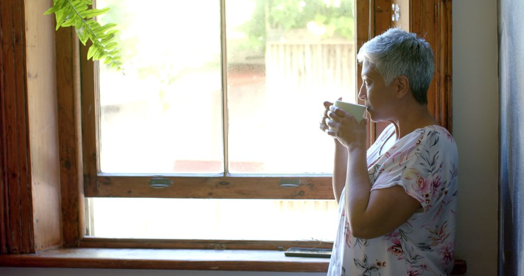 Thoughtful Elderly Woman Enjoying Tea by Window Light