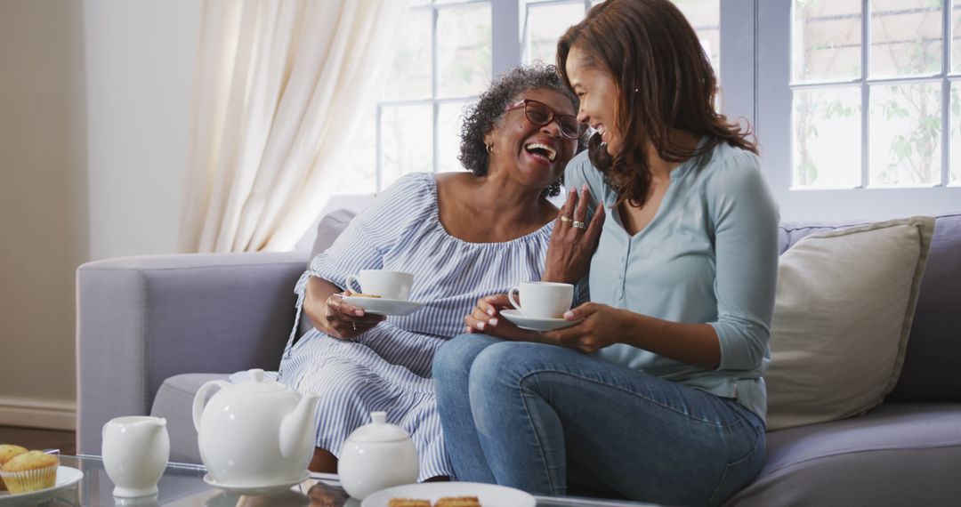 Laughing Mother and Daughter Enjoying Afternoon Tea on Sofa