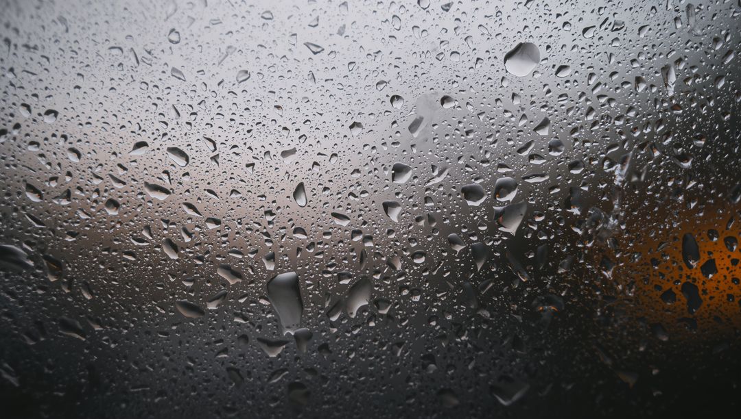 Rain-dappled windowpane showing condensation droplets and moody city bokeh lighting
