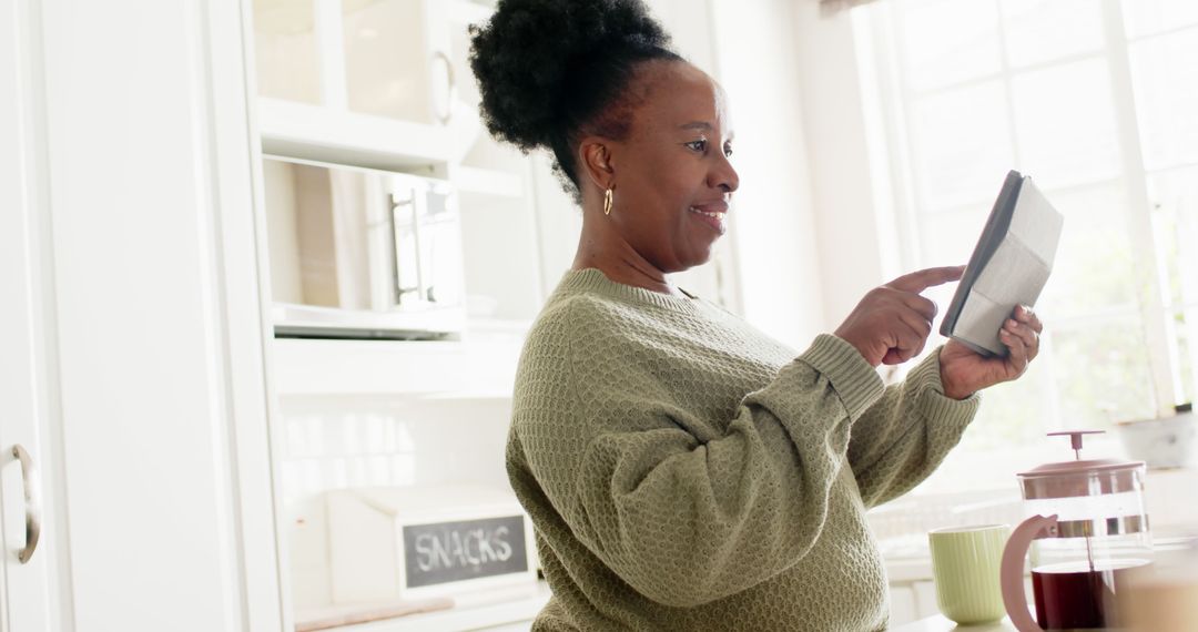 Mature African American Woman Using Tablet in Bright Kitchen - Free Images, Stock Photos and Pictures on Pikwizard.com