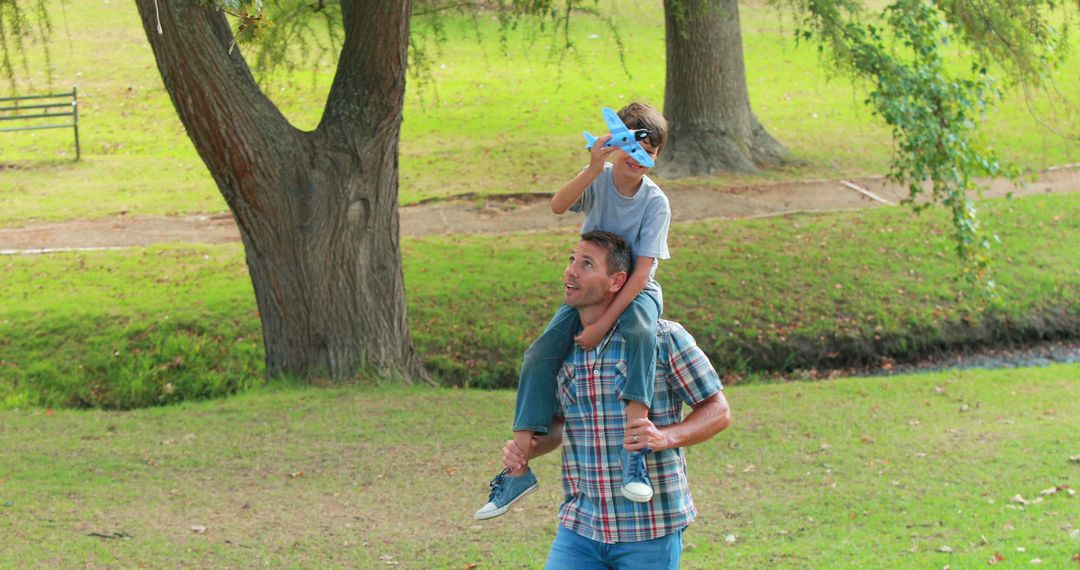 Father carrying son on shoulders while playing with toy airplane in park - Free Images, Stock Photos and Pictures on Pikwizard.com