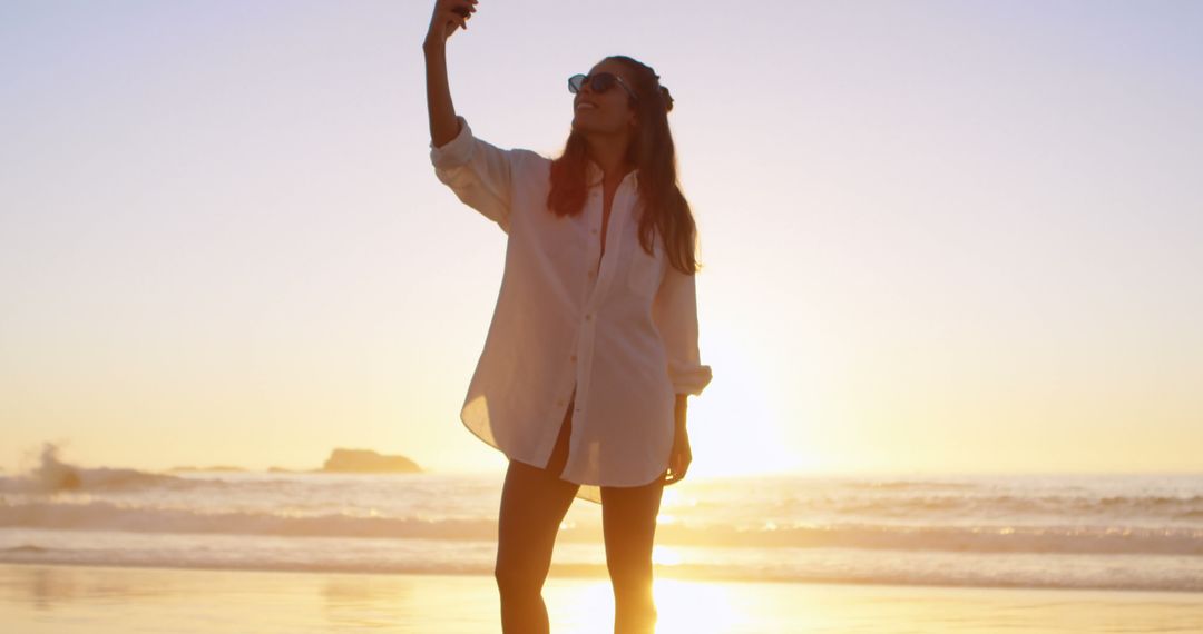 Woman Taking Selfie at Beach During Sunset in Casual Attire - Free Images, Stock Photos and Pictures on Pikwizard.com