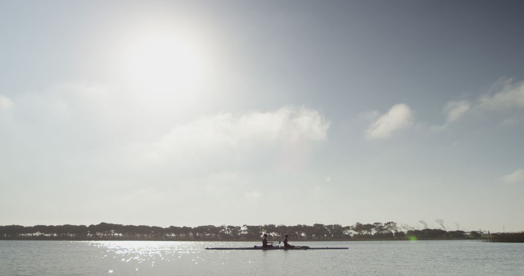 Two People Rowing Canoe on Calm Lake with Tree Line Horizon under Bright Sun - Free Images, Stock Photos and Pictures on Pikwizard.com