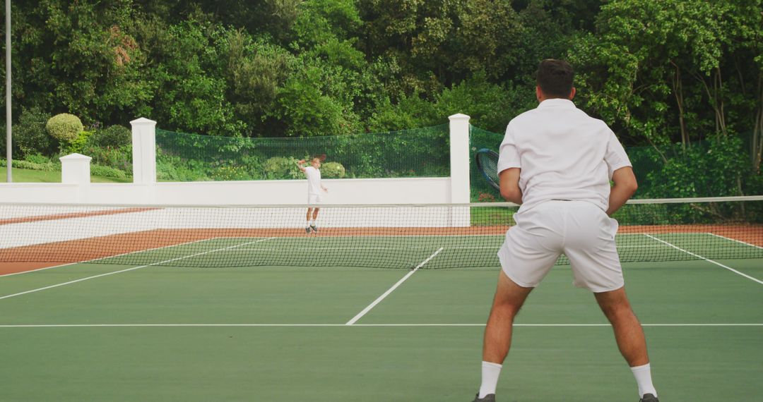 Two Men Playing Tennis on Outdoor Court Surrounded by Greenery - Free Images, Stock Photos and Pictures on Pikwizard.com