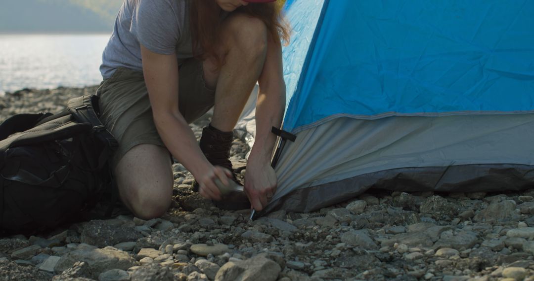 Camping enthusiast pitching tent by lakeside