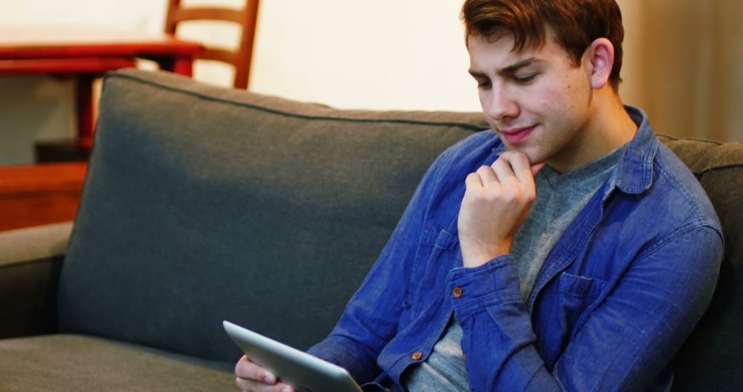 Young man browsing digital tablet on sofa at home - Free Images, Stock Photos and Pictures on Pikwizard.com