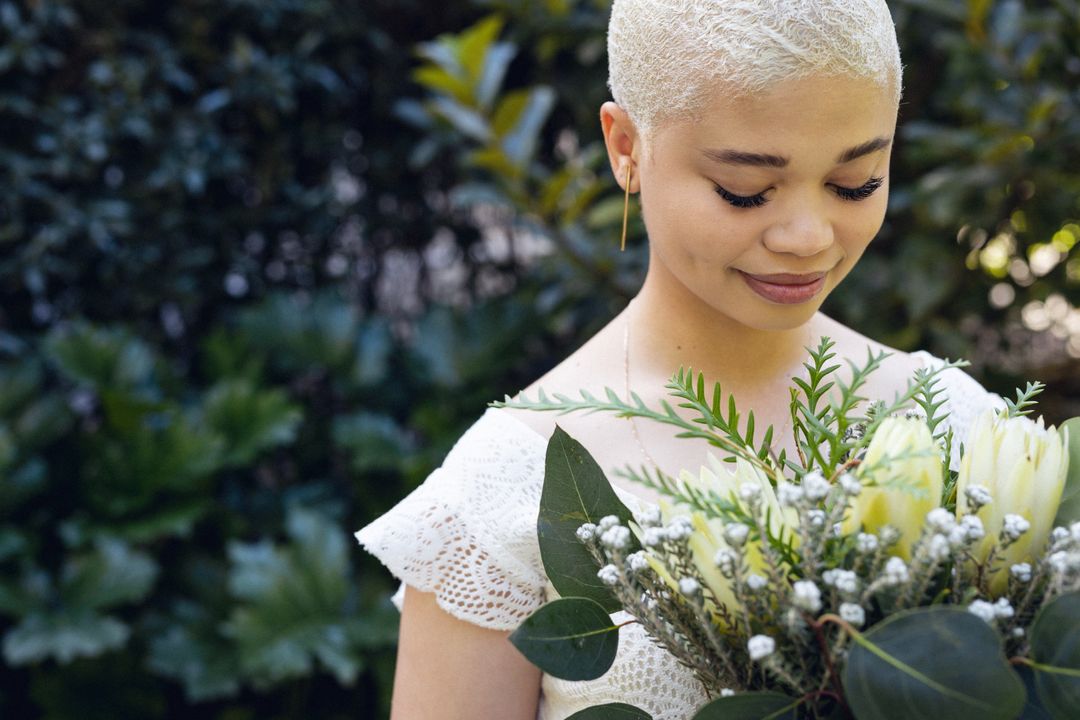 Close-up of smiling biracial young woman with short hair looking at flowers against plants in yard - Free Images, Stock Photos and Pictures on Pikwizard.com