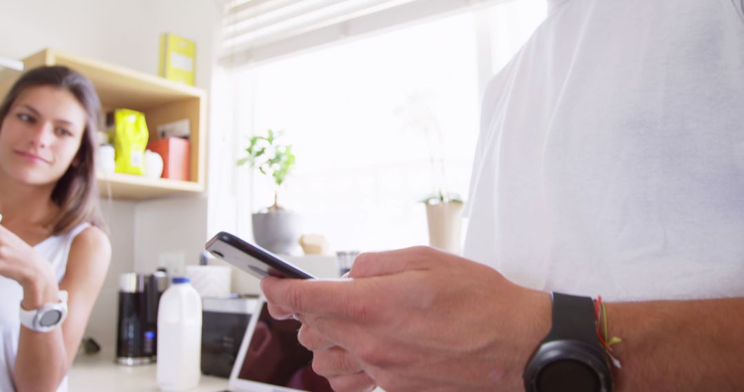 Man using smartphone with observing woman in kitchen interior