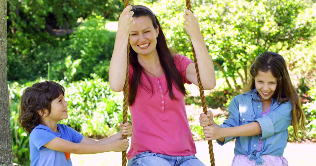 Children pushing their mother on a swing in the park on a sunny day - Free Images, Stock Photos and Pictures on Pikwizard.com