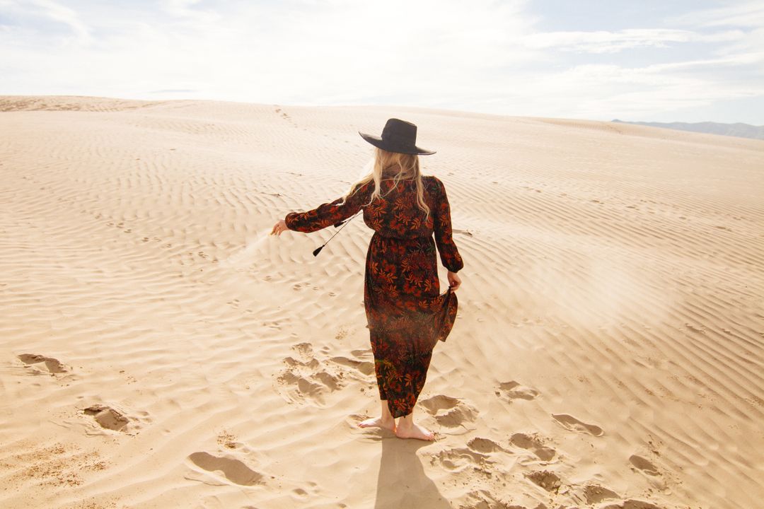 Woman Walking in Desert Sand Dunes in Flowing Dress and Hat - Free Images, Stock Photos and Pictures on Pikwizard.com