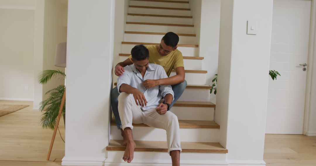 Smiling biracial gay male couple sitting on stairs holding hands embracing and talking - Free Images, Stock Photos and Pictures on Pikwizard.com