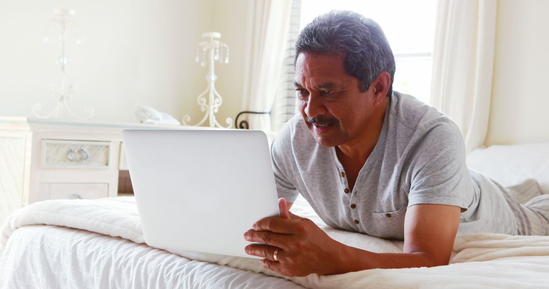 Middle-Aged Man Using Laptop on Bed in Cozy Bedroom - Free Images, Stock Photos and Pictures on Pikwizard.com