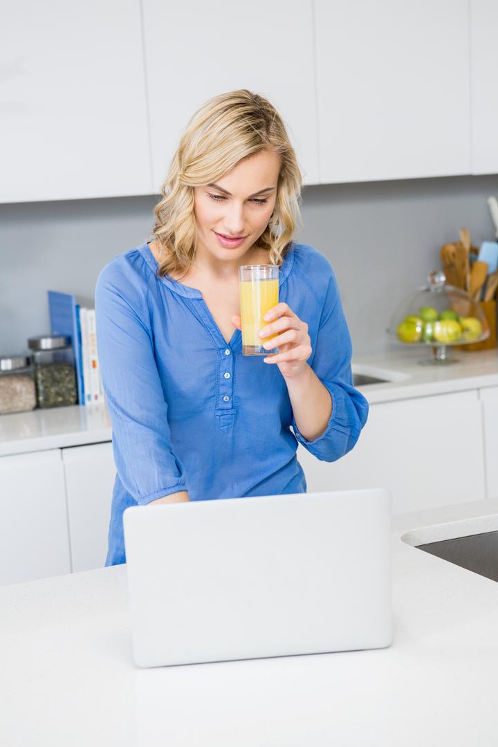 Woman Holding Juice and Using Laptop in Modern Kitchen - Free Images, Stock Photos and Pictures on Pikwizard.com