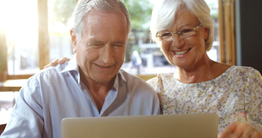 Senior Couple Laughing While Using Laptop in Cafe