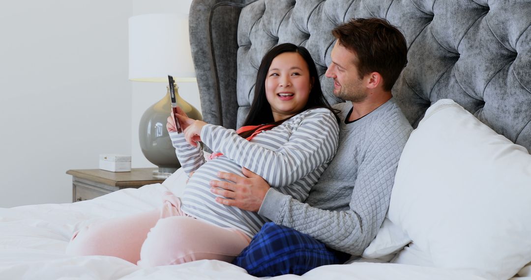 Expectant Parents Relaxing in Bed with Tablet, Smiling Happily - Free Images, Stock Photos and Pictures on Pikwizard.com