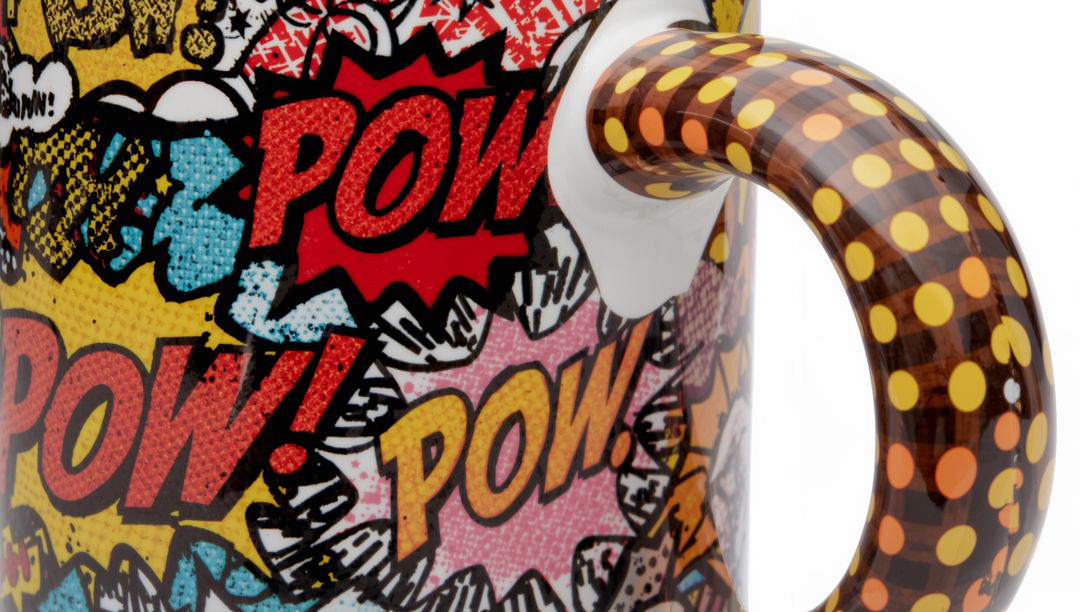 Glossy ceramic mug featuring pop art POW bursts and brown polka-dot handle, close-up white backdrop