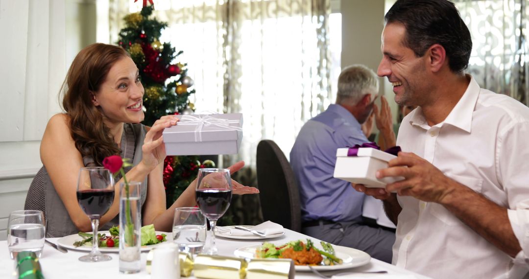 Couple Exchanging Gifts During Christmas Dinner at Restaurant - Free Images, Stock Photos and Pictures on Pikwizard.com