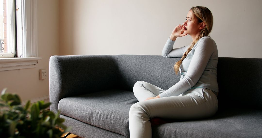 Contemplative Young Woman Sitting on Sofa in Modern Living Room - Free Images, Stock Photos and Pictures on Pikwizard.com