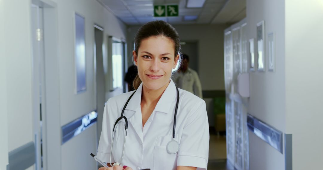 Smiling Female Healthcare Worker in Hospital Corridor with Clipboard and Stethoscope - Free Images, Stock Photos and Pictures on Pikwizard.com