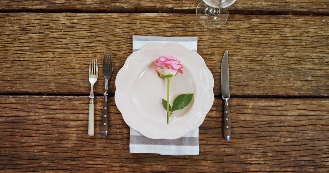 A pink flower adorns a white plate set with cutlery on a rustic wooden table, with copy space - Free Images, Stock Photos and Pictures on Pikwizard.com