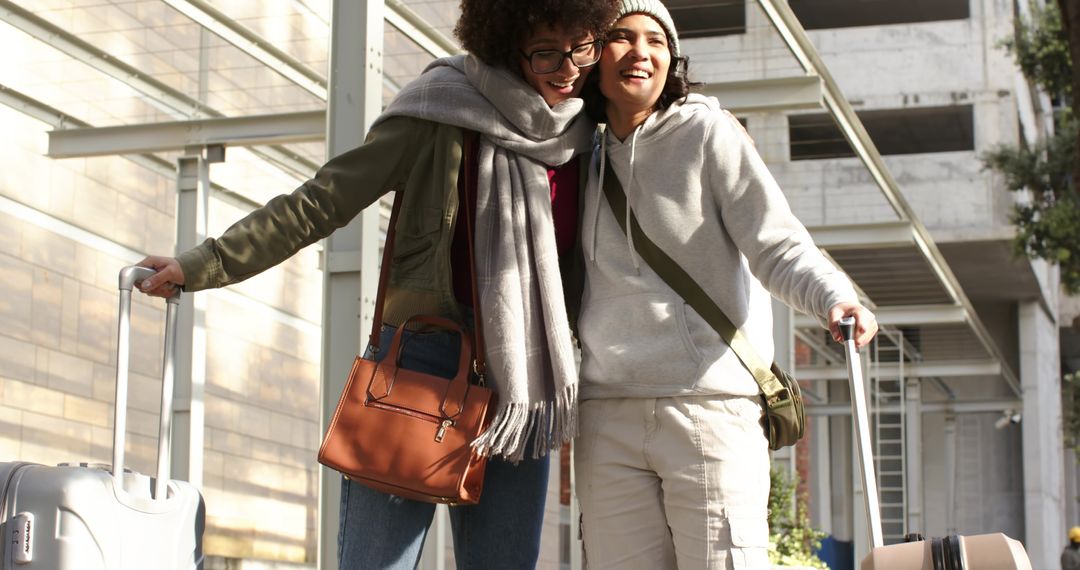 Friends laughing while traveling with rolling suitcases under urban glass canopy