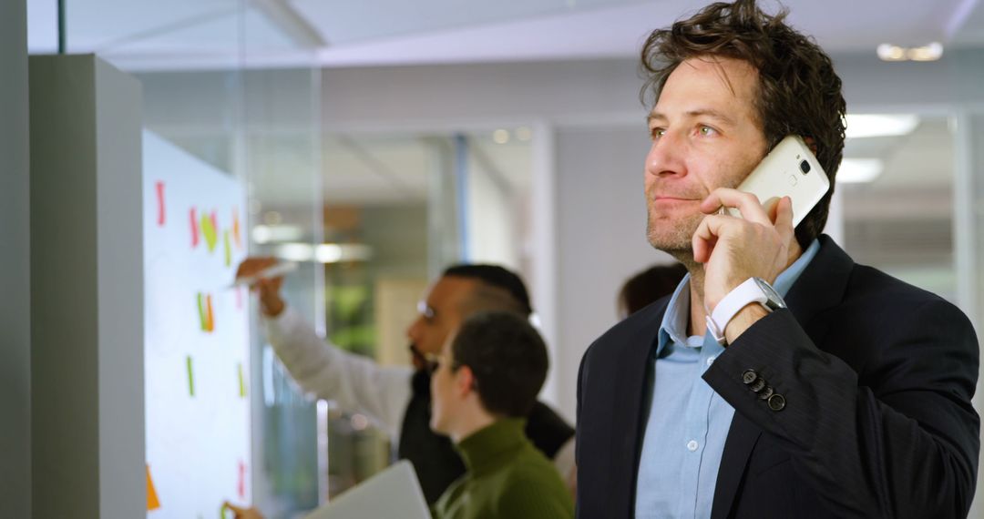 Businessman Discussing Ideas on Phone in Modern Office With Colleagues - Free Images, Stock Photos and Pictures on Pikwizard.com